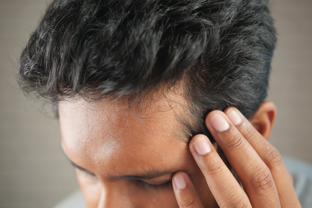 Close-up of a man's hand touching his head in contemplation. Neutral tones and soft lighting.