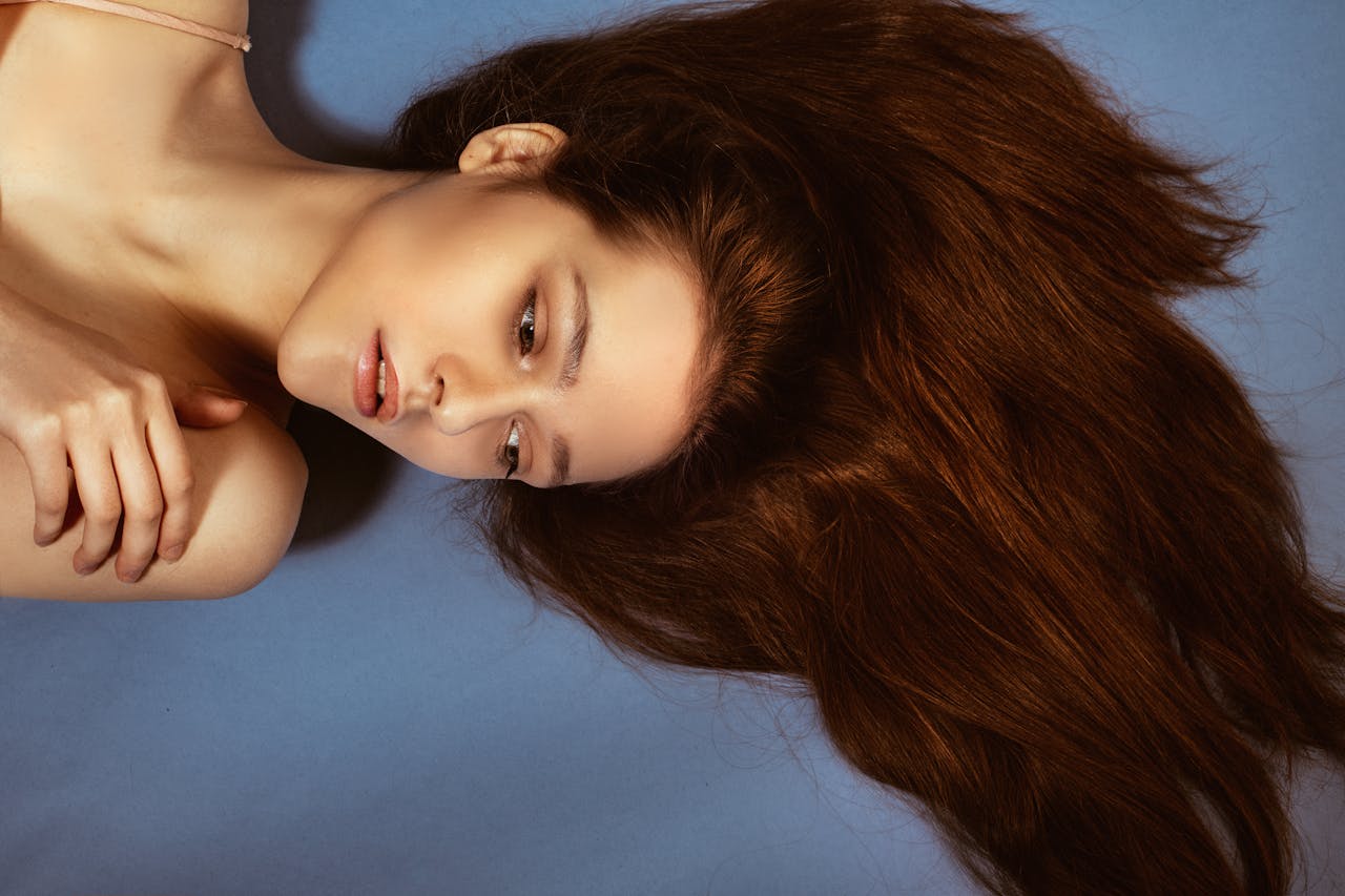 Close-up portrait of a woman with long hair lying on a blue surface, showcasing elegance and beauty.