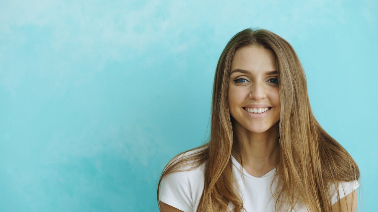 Portrait of a smiling woman with long hair against a blue backdrop.
