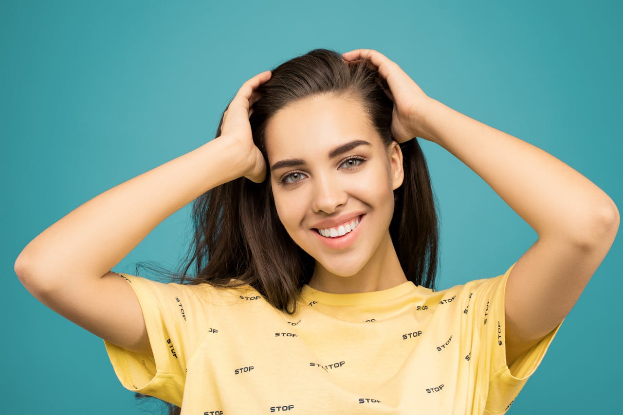 Portrait of a happy woman in a yellow shirt against a teal background.