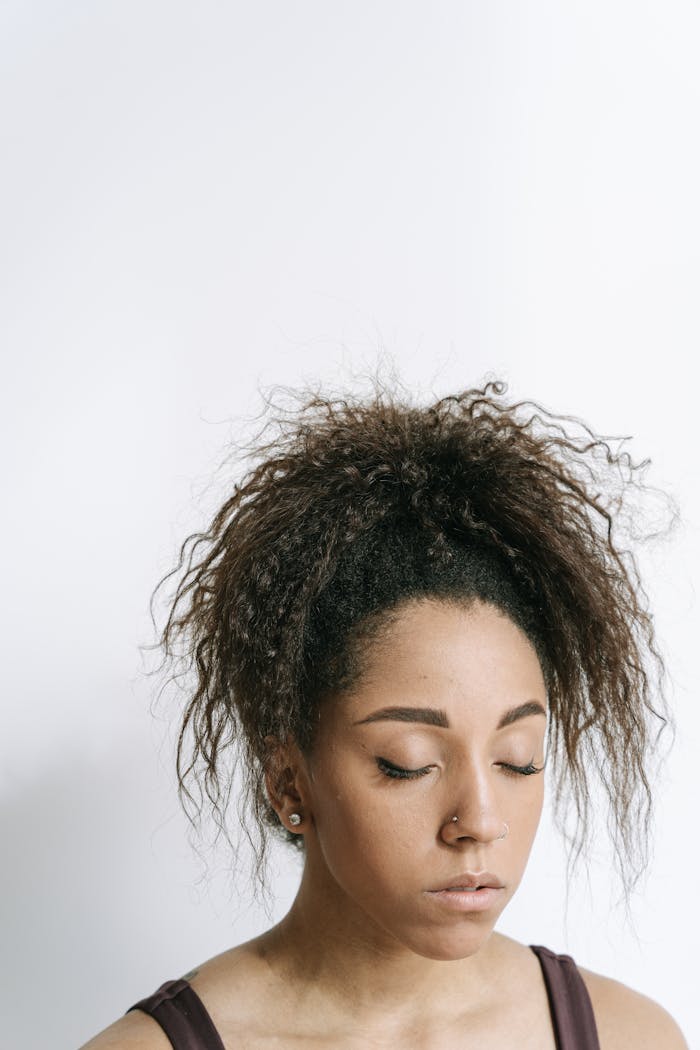A serene portrait of a young woman with curly hair meditating peacefully with her eyes closed.